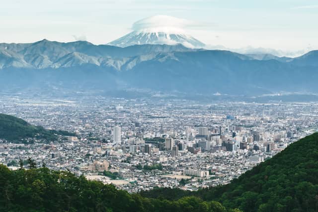 El monte Fuji con una nube lenticular en la cima, sobre una cordillera y una gran ciudad